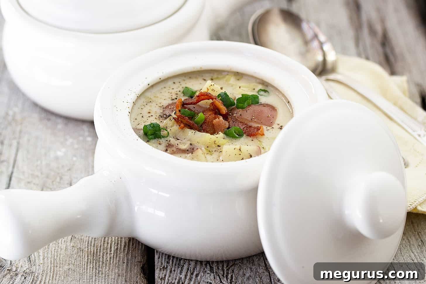 Two white soup bowls filled with hearty Irish Colcannon Soup, garnished with crispy bacon and fresh green onions.