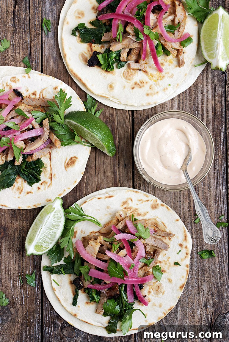 Close-up of freshly assembled Porchetta Tacos garnished with blanched broccoli rabe, bright pickled red onions, and a generous drizzle of chipotle mayo, showcasing their irresistible layers.