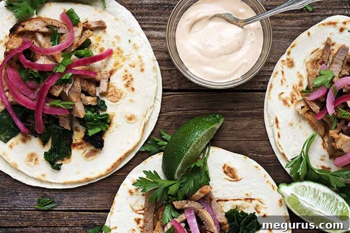 Delicious porchetta tacos arranged artfully on a serving platter, topped with fresh herbs and lime wedges.