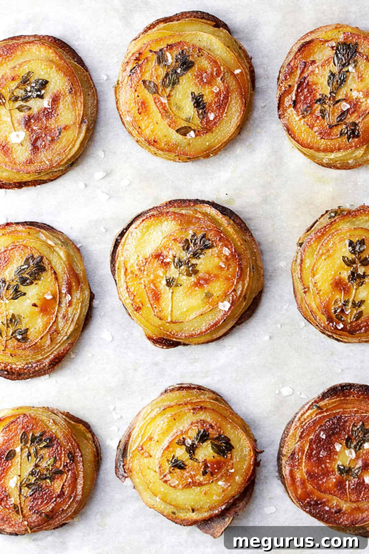Close-up of baked Mini Pommes Anna on parchment paper, showing crispy edges and layered texture.