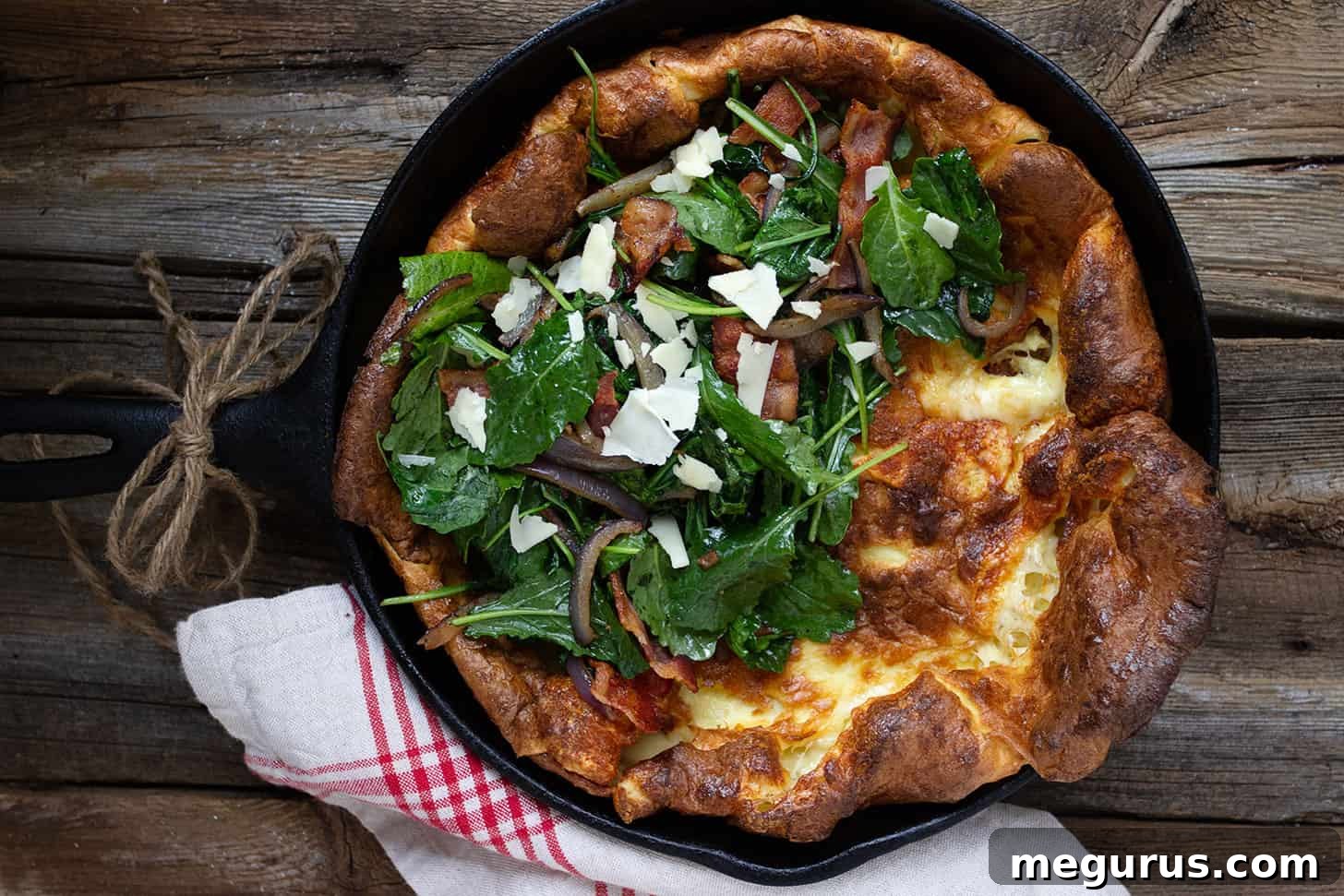 Crispy bacon Dutch baby with vibrant greens and melted cheese, freshly baked in a cast iron skillet.