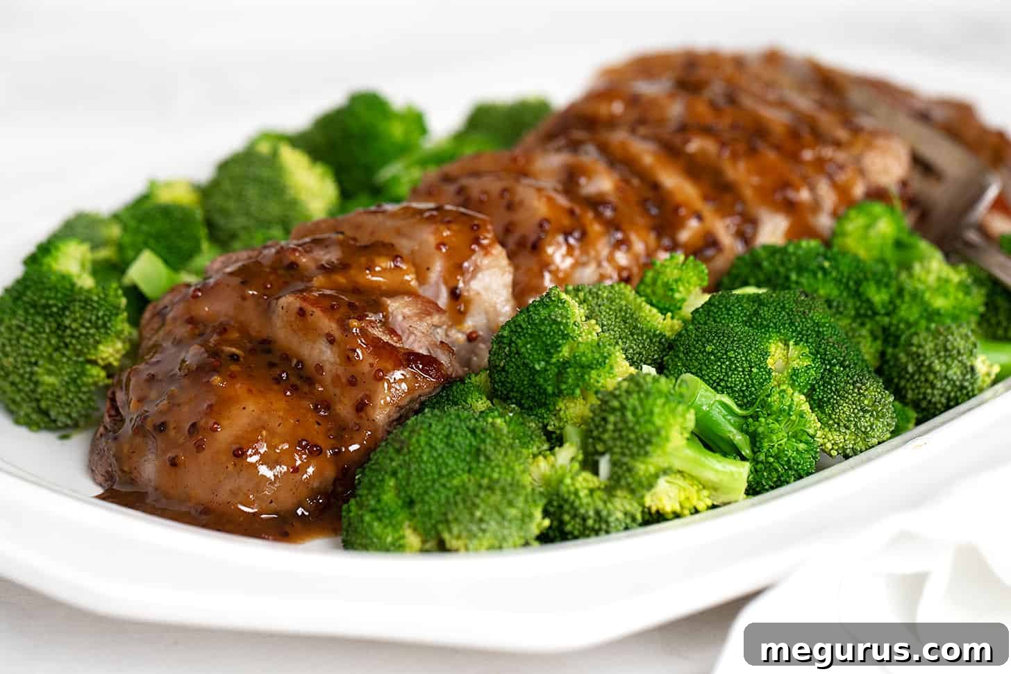 Perfectly sliced maple mustard pork tenderloin on a plate with fresh broccoli, generously drizzled with the savory pan sauce