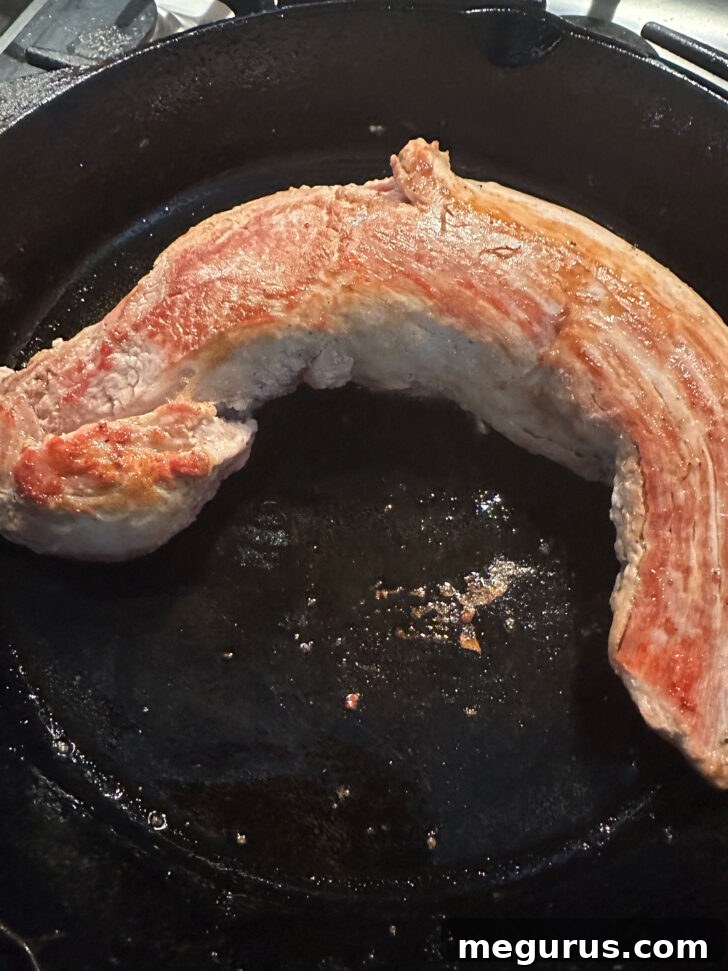 Pork tenderloin being browned in a hot cast iron skillet on the stove-top