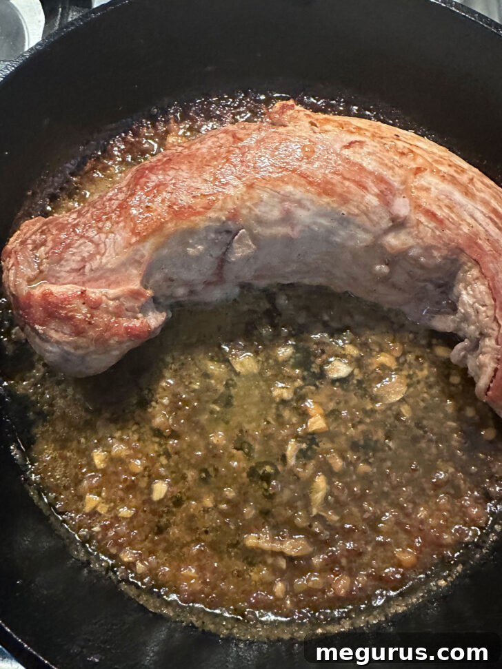 The skillet, with pork tenderloin bathed in sauce, prepared for oven roasting