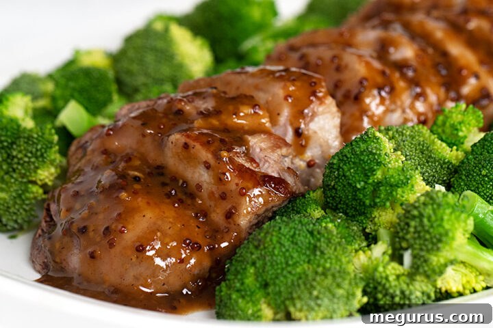 Beautifully plated maple mustard pork tenderloin, sliced and served with a side of steamed broccoli, drizzled with pan sauce