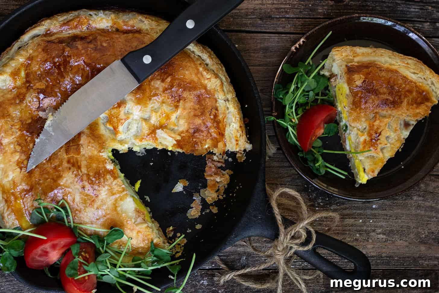Golden brown skillet bacon and egg pie with a slice on a plate, showcasing its flaky puff pastry crust and savory filling.