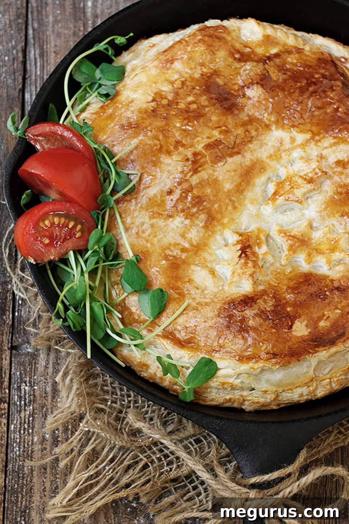 Close-up of a golden-baked bacon and egg pie in a cast iron skillet, showing the crispy pastry and visible egg and bacon filling.