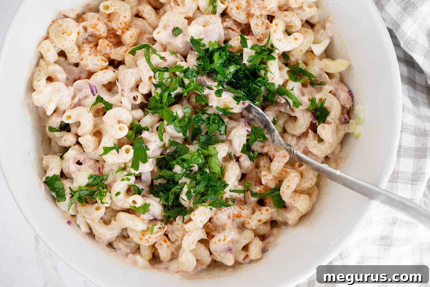 A large bowl of classic tuna pasta salad with a serving spoon, garnished with fresh parsley.