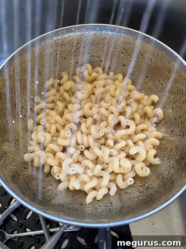 Cooked pasta being rinsed under cold water in a colander to stop the cooking process.