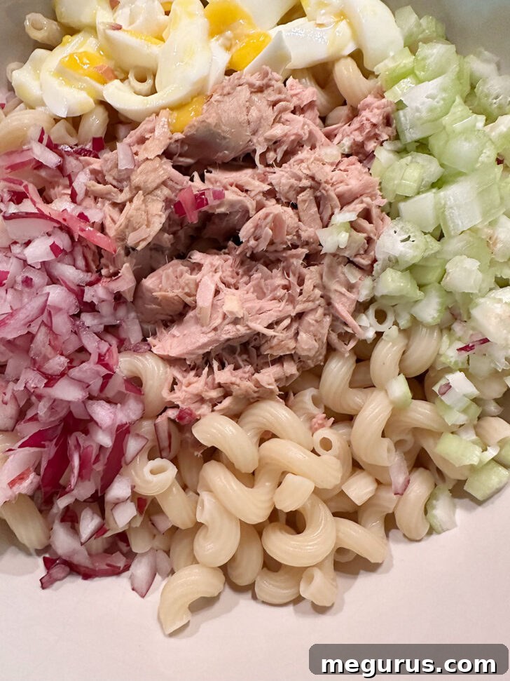 All solid ingredients for tuna pasta salad, including pasta, tuna, celery, red onion, and chopped eggs, in a large bowl.