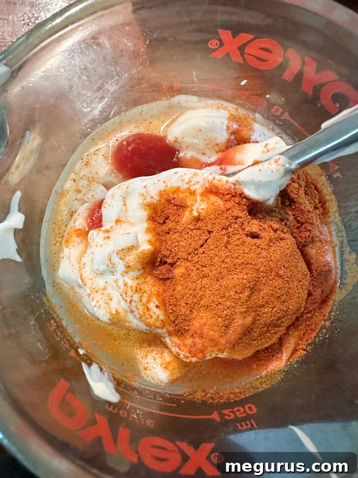 Ingredients for the salad dressing, including mayonnaise, ketchup, sour cream, paprika, and white vinegar, mixed in a measuring cup.