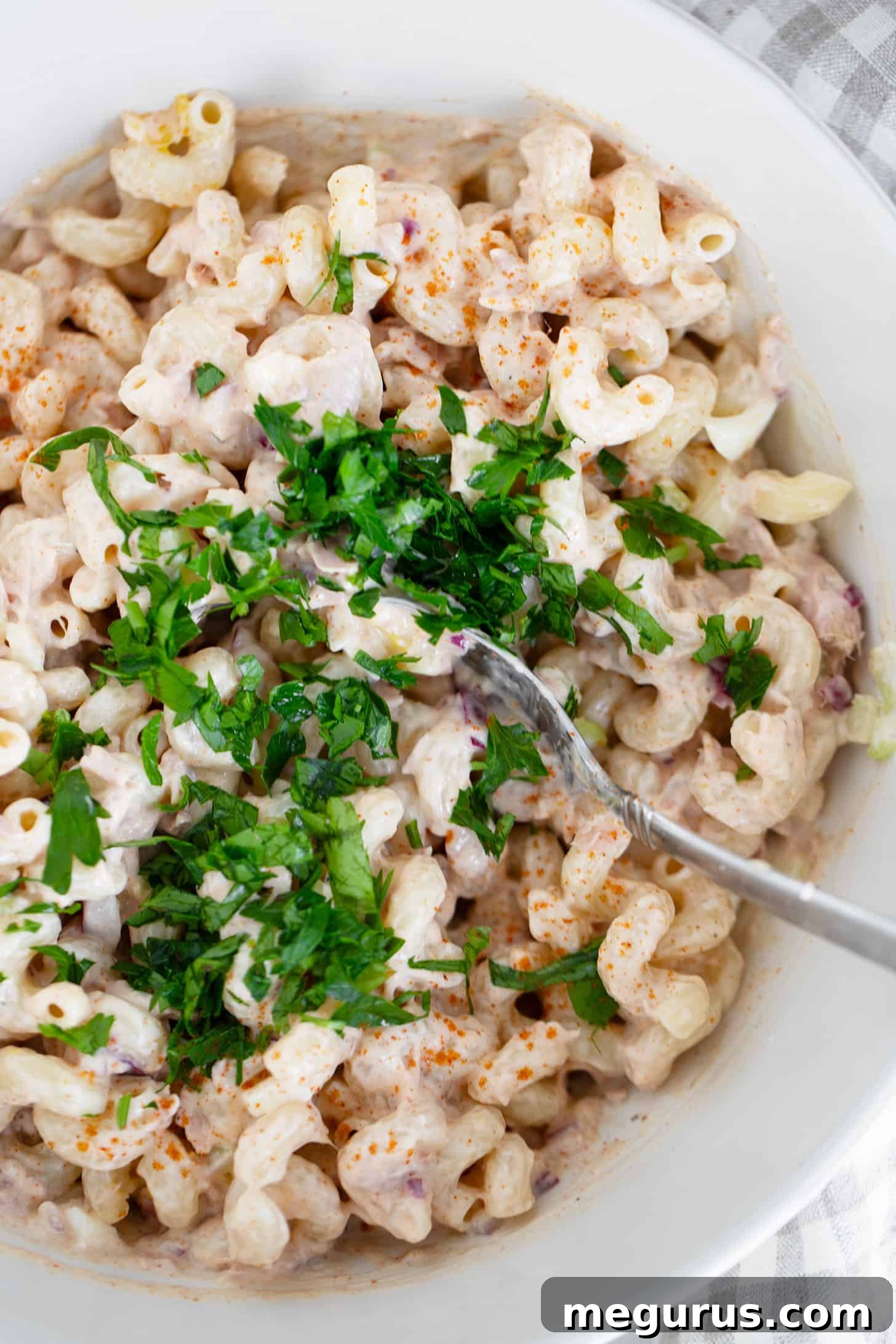 Close-up of a serving of tuna pasta salad in a bowl with a fork, showing the creamy texture and ingredients.