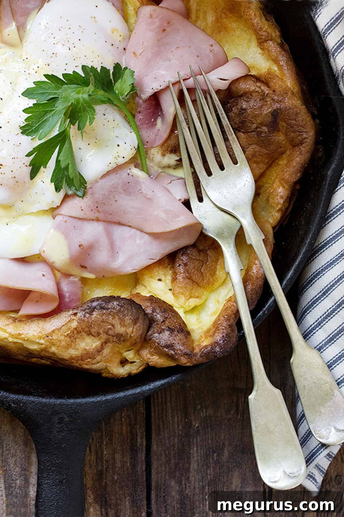 Close-up of the puffy edges of an Eggs Benedict Dutch Baby with perfectly cooked ham and poached eggs, illustrating the rich texture.