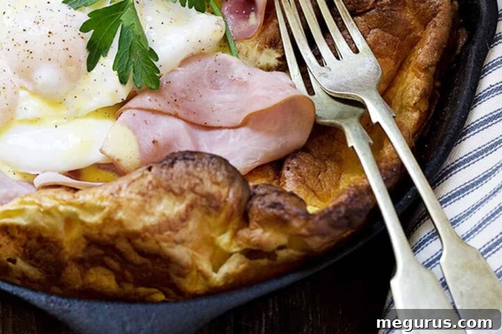 A stunning Eggs Benedict Dutch Baby in a cast iron skillet, garnished with fresh parsley.