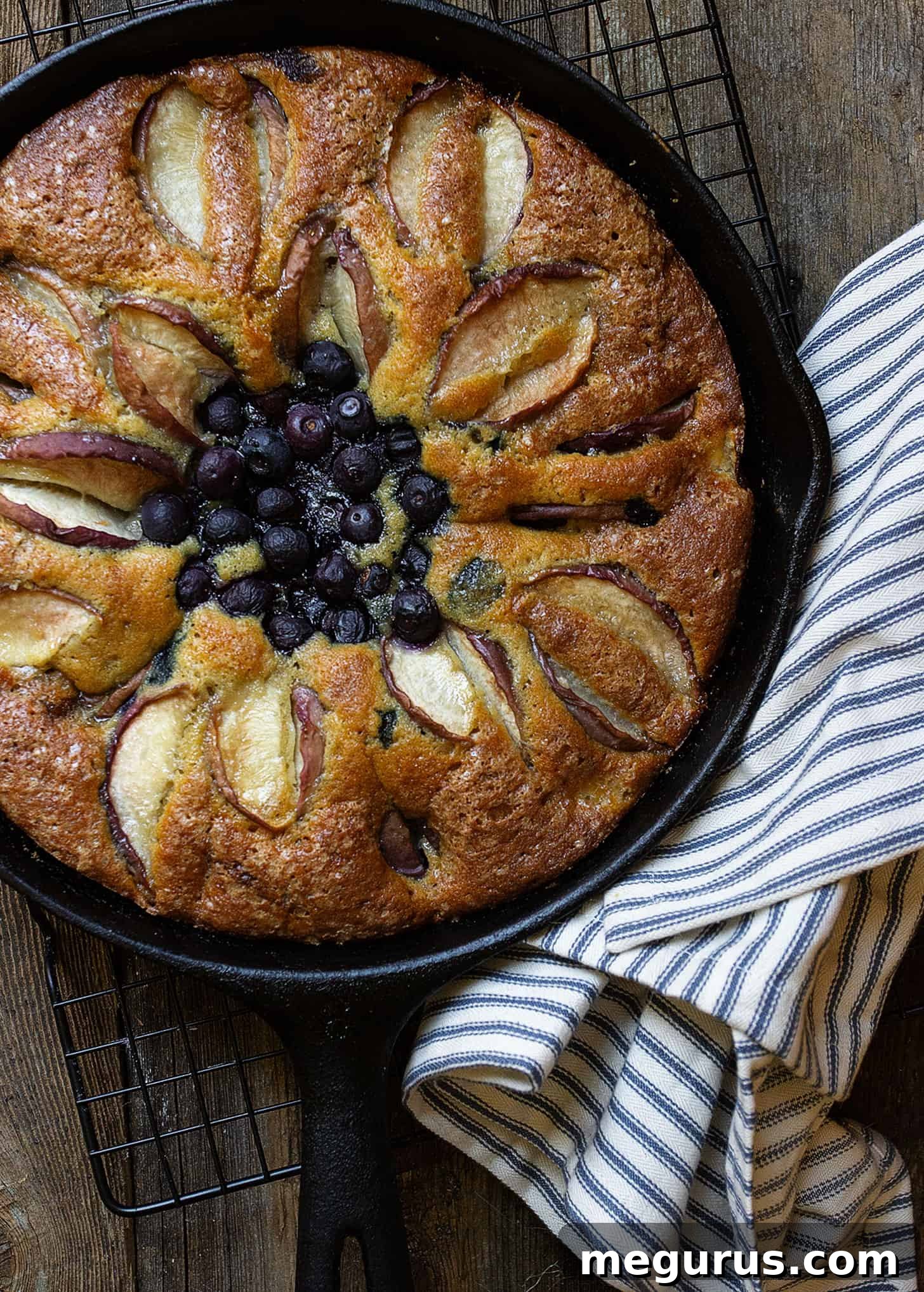overhead shot of a golden-brown blueberry peach skillet cake, with peaches arranged in a decorative pattern