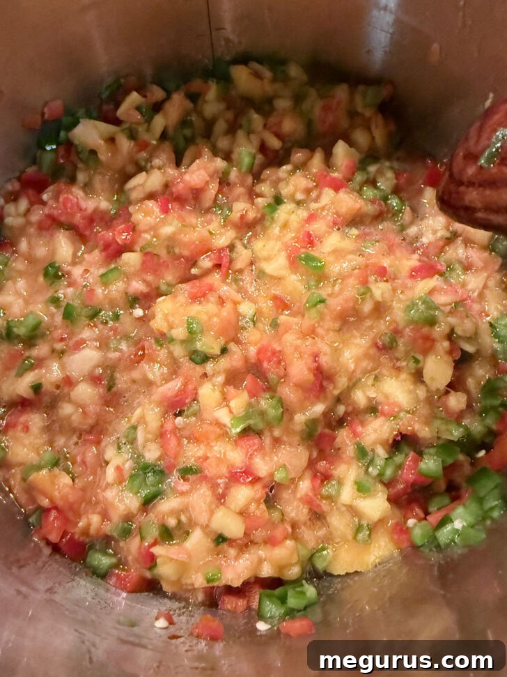 Finely chopped peaches, jalapeños, and bell peppers combined in a large cooking pot.