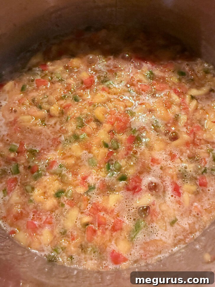 The peach and pepper mixture reaching a full boil in the pot, before adding sugar.