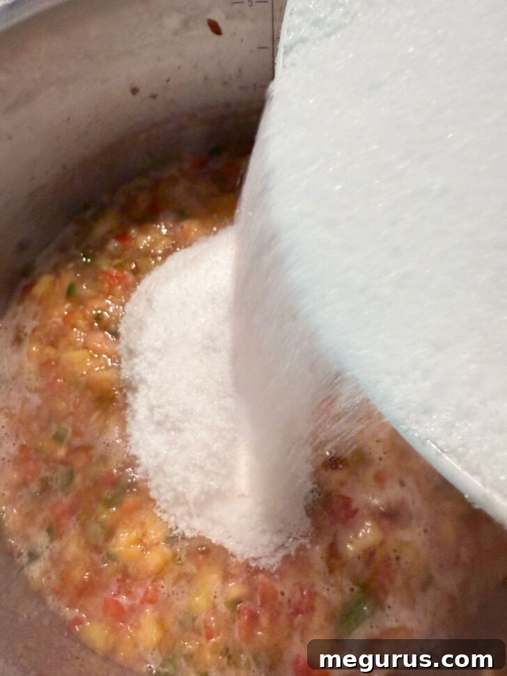 Granulated sugar being added to the boiling peach and pepper jam mixture.