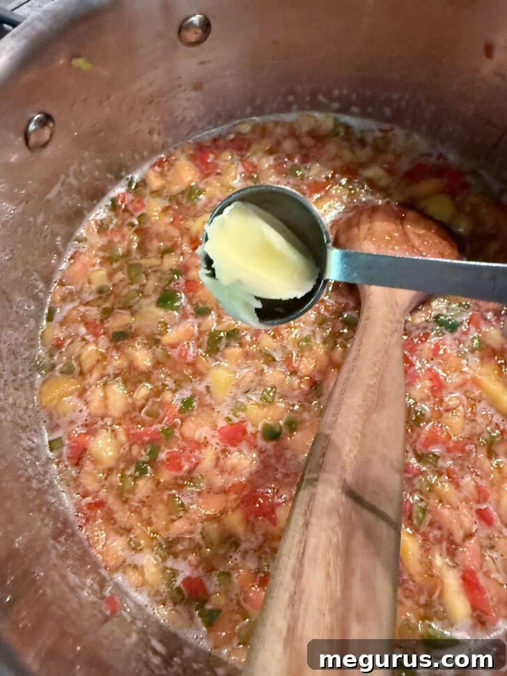A small pat of butter being added to the boiling jam mixture to reduce foam.