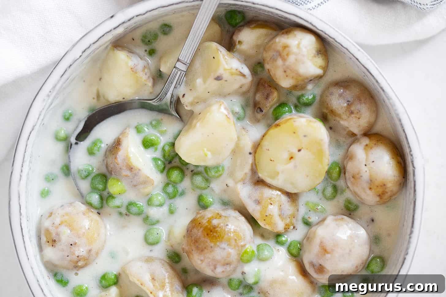 Creamed peas and potatoes in serving dish with spoon.