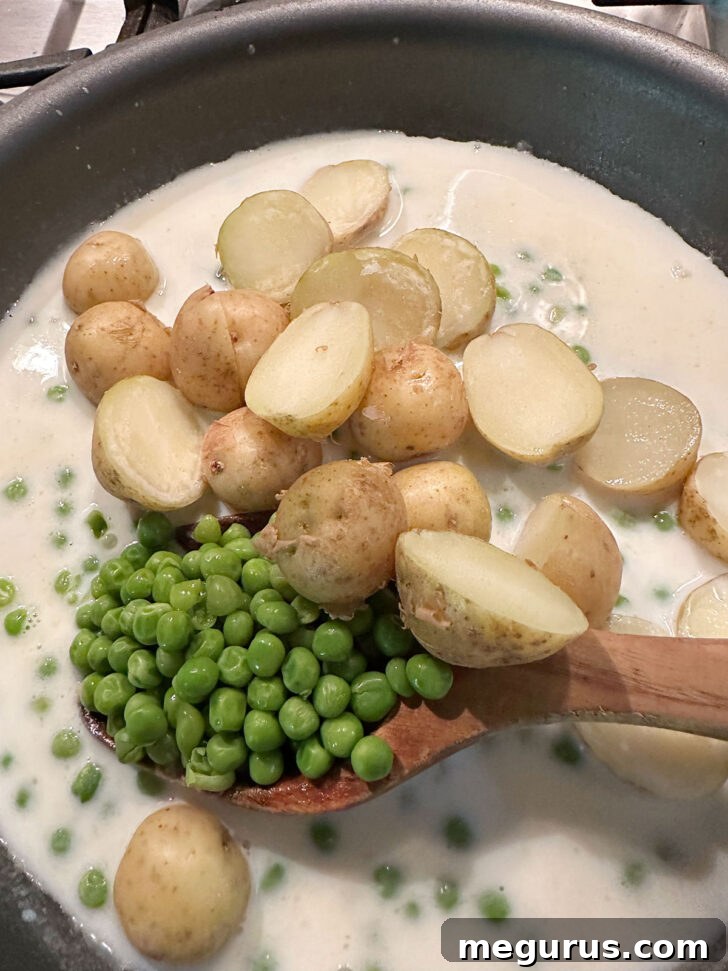 Cooked peas and potatoes added to white sauce in skillet.