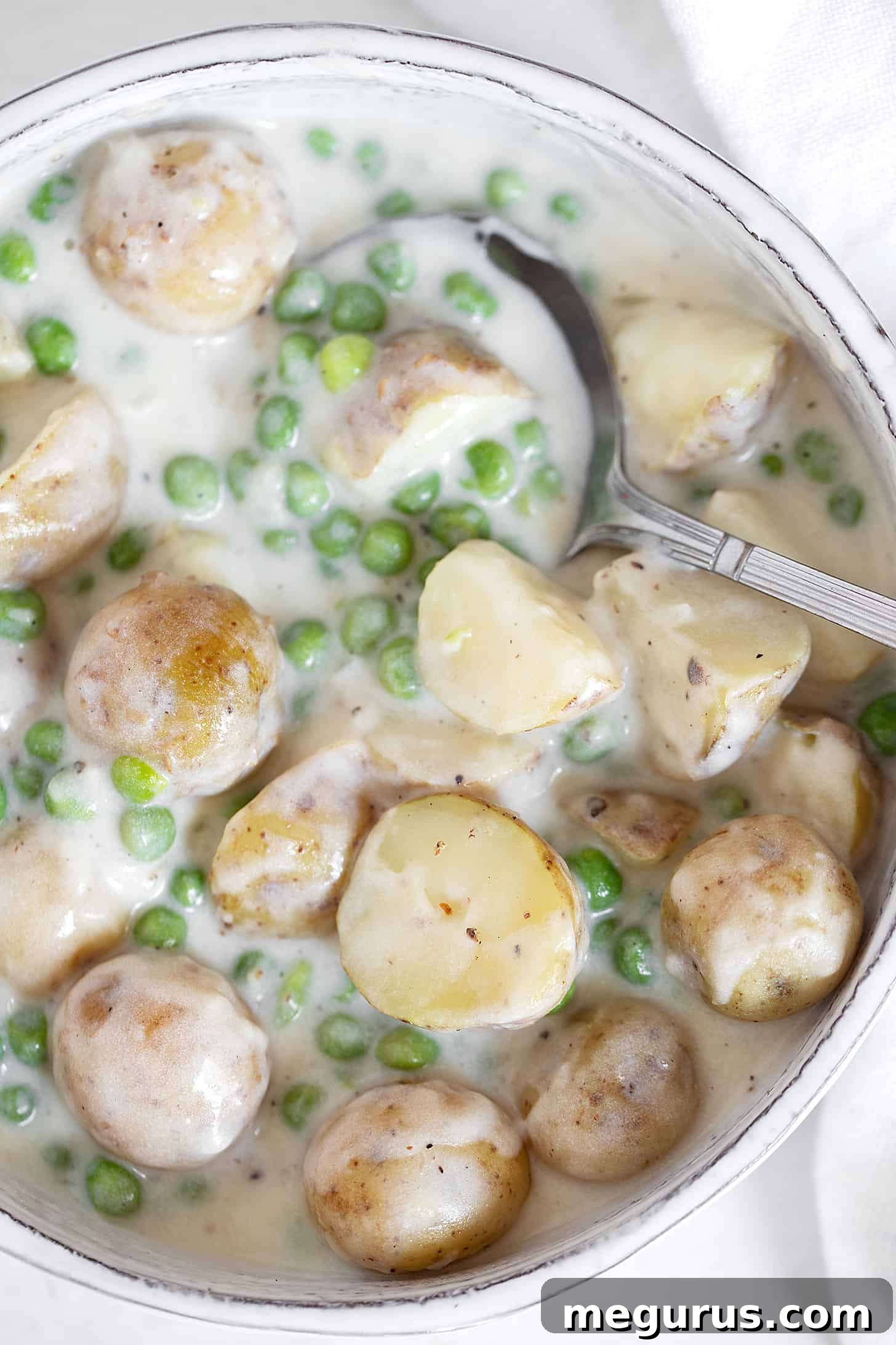 Creamed peas and potatoes in serving dish with spoon.