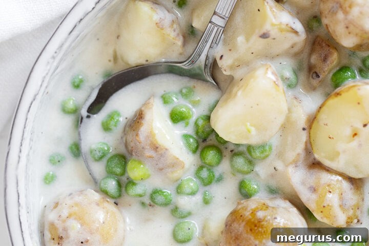 Creamed peas and potatoes in serving dish with spoon.