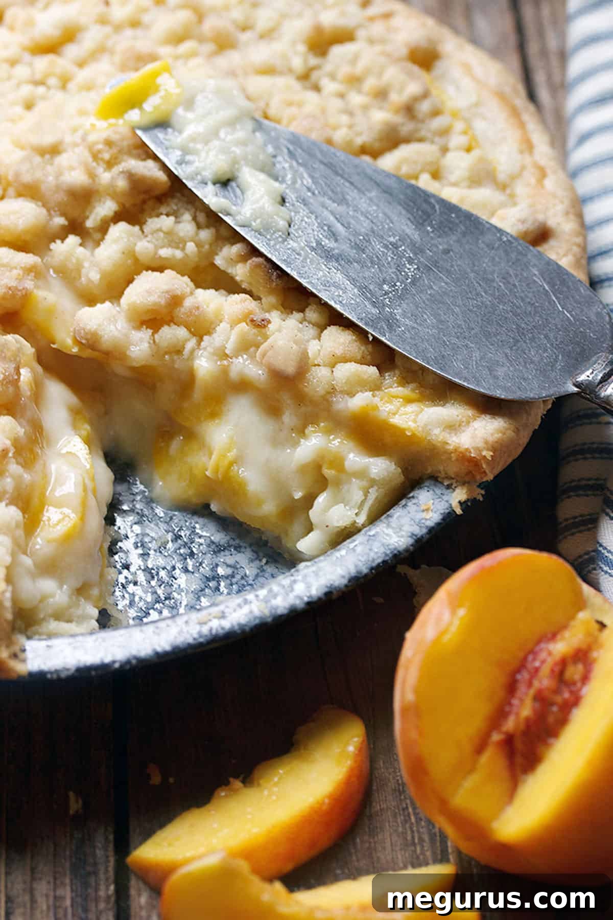 A slice of peaches and cream pie on a plate, showing the layered filling and golden crumble