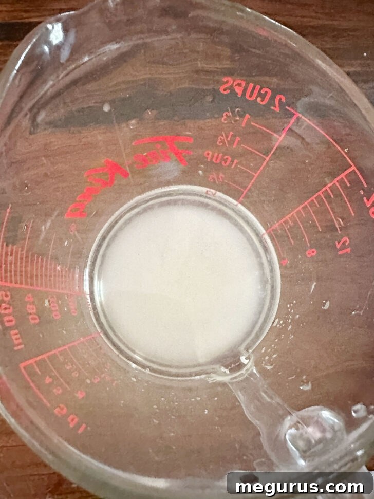 Lemon sugar syrup, a clear golden liquid, in a glass measuring cup before being heated, showing its readiness.