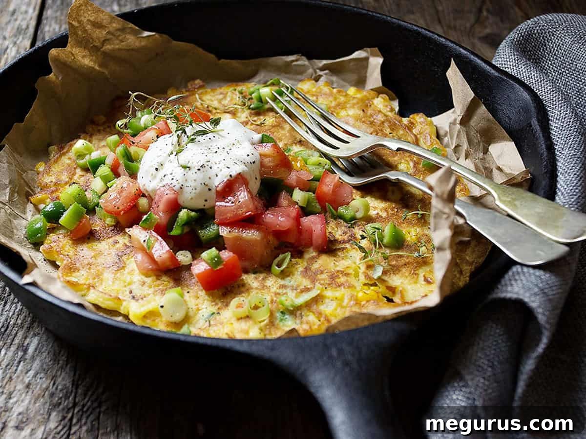 Crispy savoury corn pancake in a cast iron skillet, beautifully garnished with vibrant fresh jalapeños and diced tomatoes, offering a tantalizing visual of a delicious meal ready to be served.