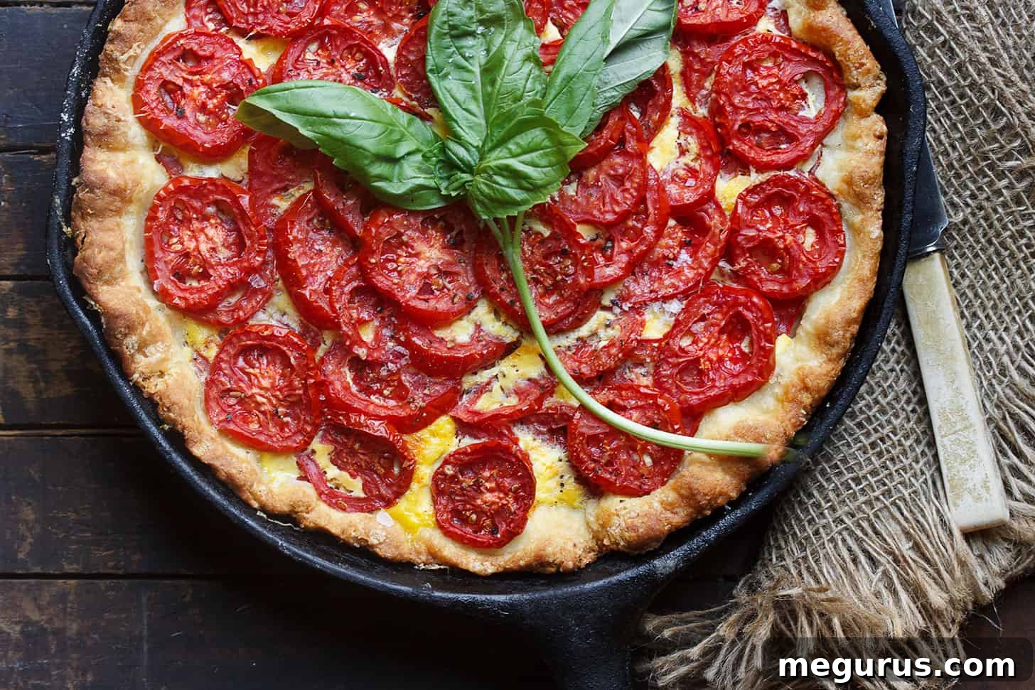 Golden brown tomato cheese pie with basil leaves in a cast iron skillet, ready to be served.