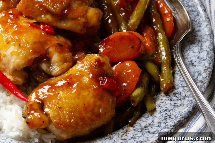 Sweet and Sour Chicken Thighs on a plate with rice and green beans, garnished with sesame seeds