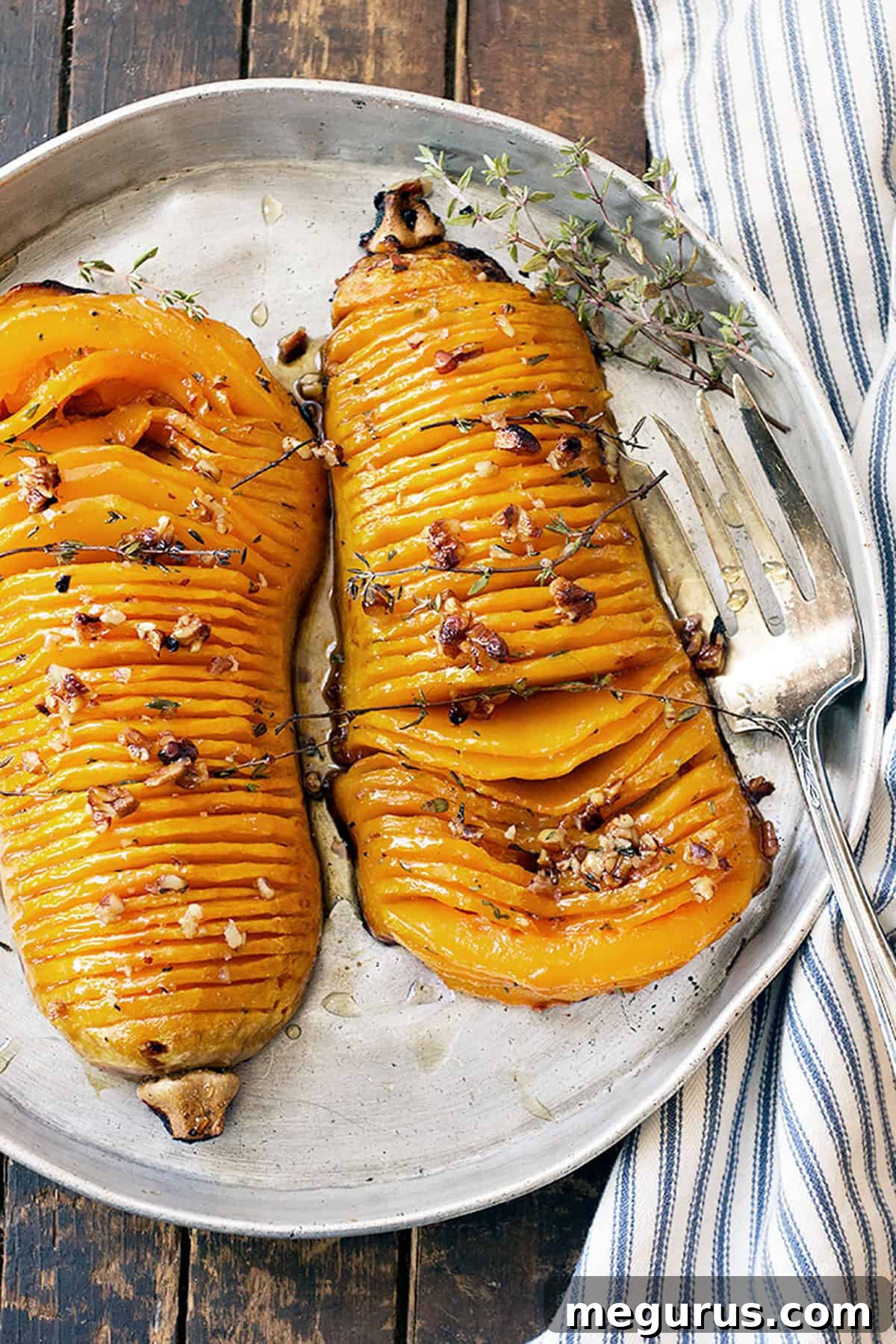 Beautifully roasted Hasselback butternut squash halves drizzled with maple glaze and garnished with fresh thyme