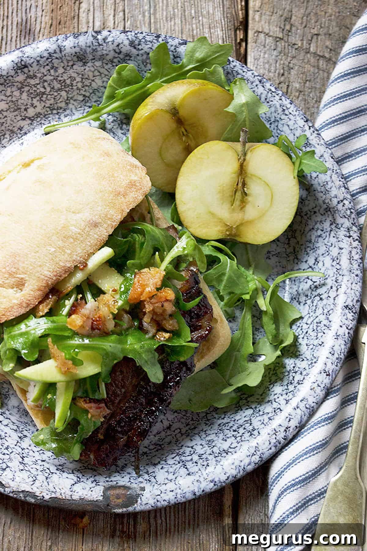 Close-up of a prepared pork belly sandwich with fresh apple and arugula on top.