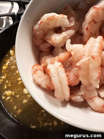 Adding shrimp to the skillet with the garlic and chicken broth.