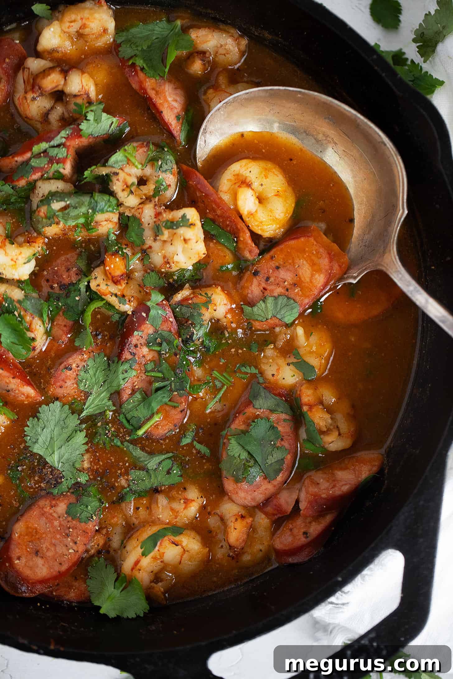 Close-up of spicy chorizo and shrimp in a cast iron skillet with a serving spoon, highlighting the rich texture.