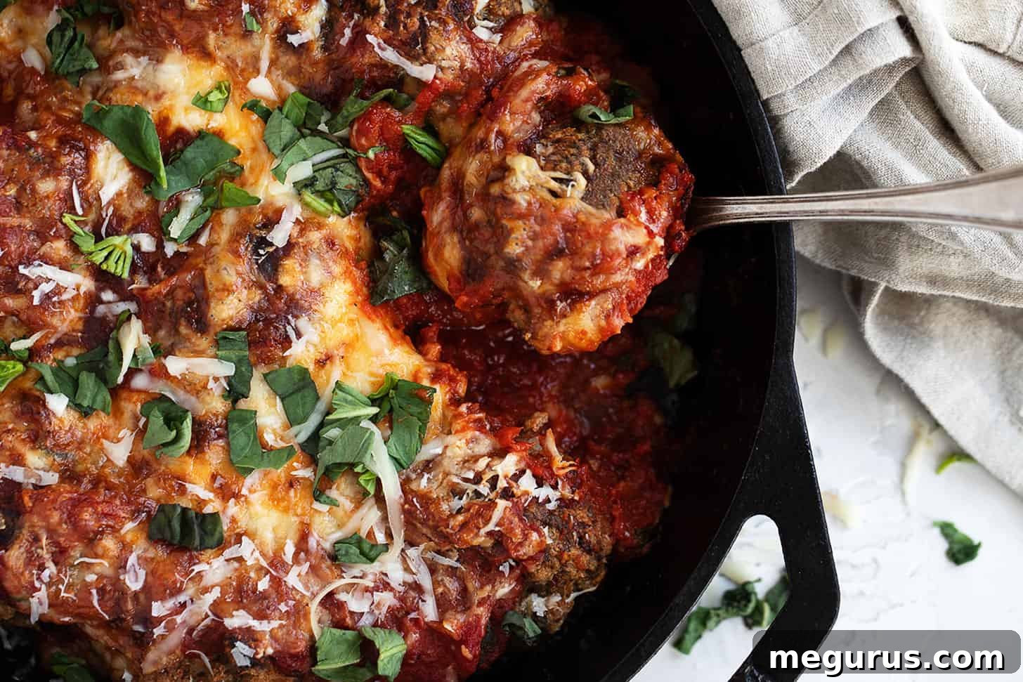 cheesy baked meatballs and tomato sauce in skillet with spoon