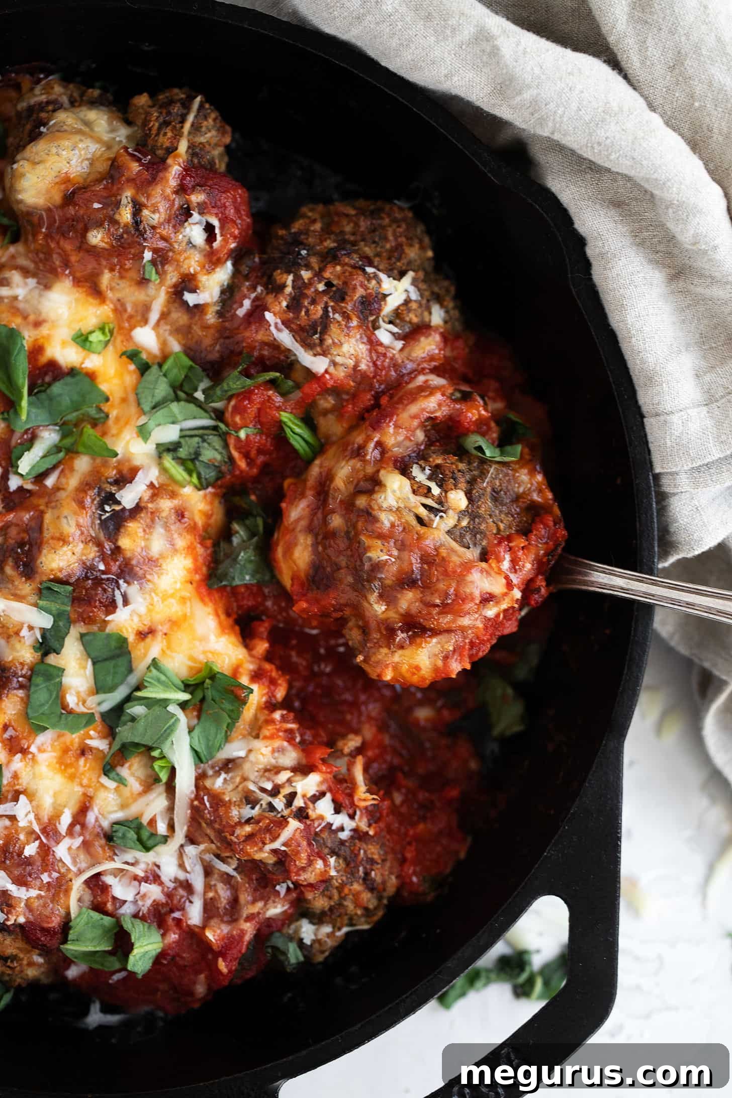 cheesy baked meatballs and tomato sauce in skillet with spoon