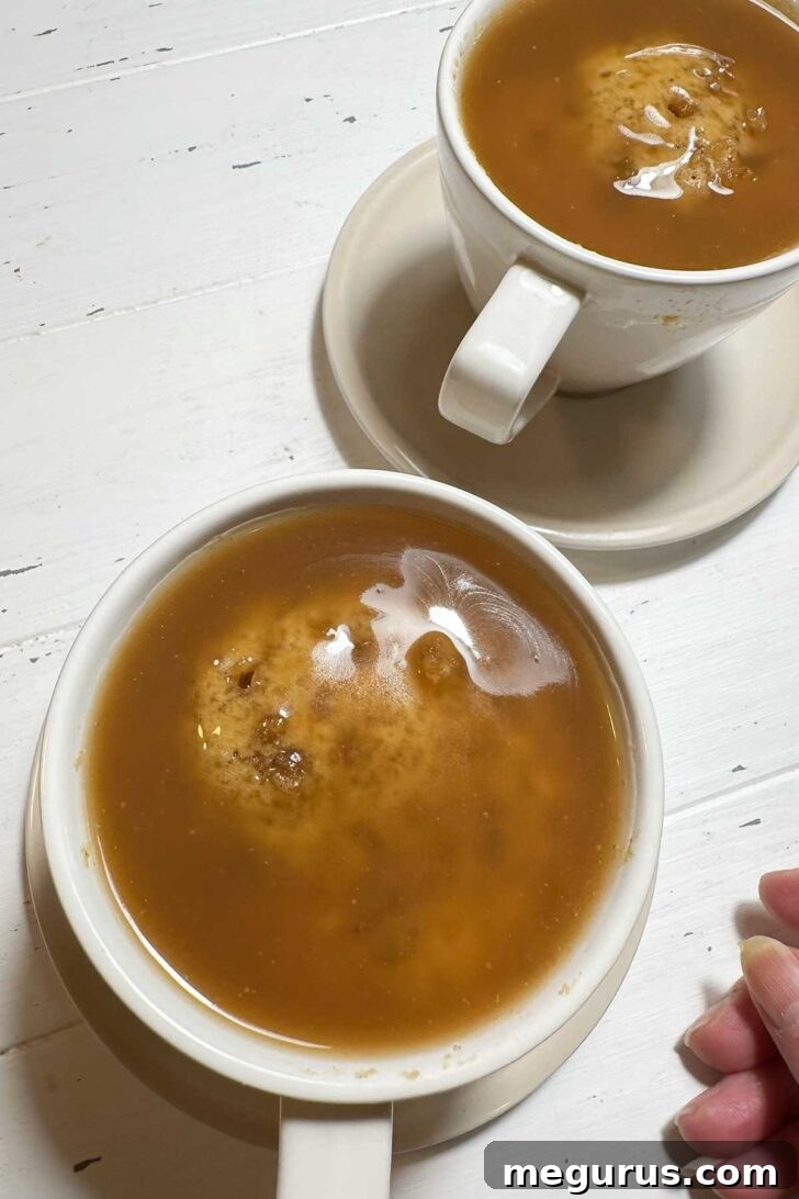 Two finished sticky toffee puddings in coffee cups, drenched in warm toffee sauce