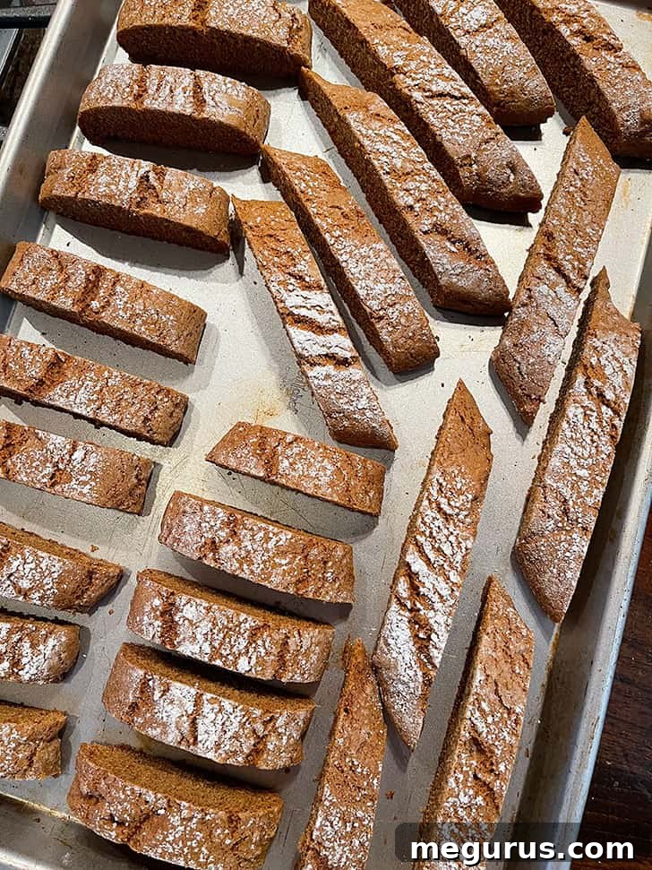 Sliced gingerbread biscotti arranged on a baking sheet, upright, for the second bake.