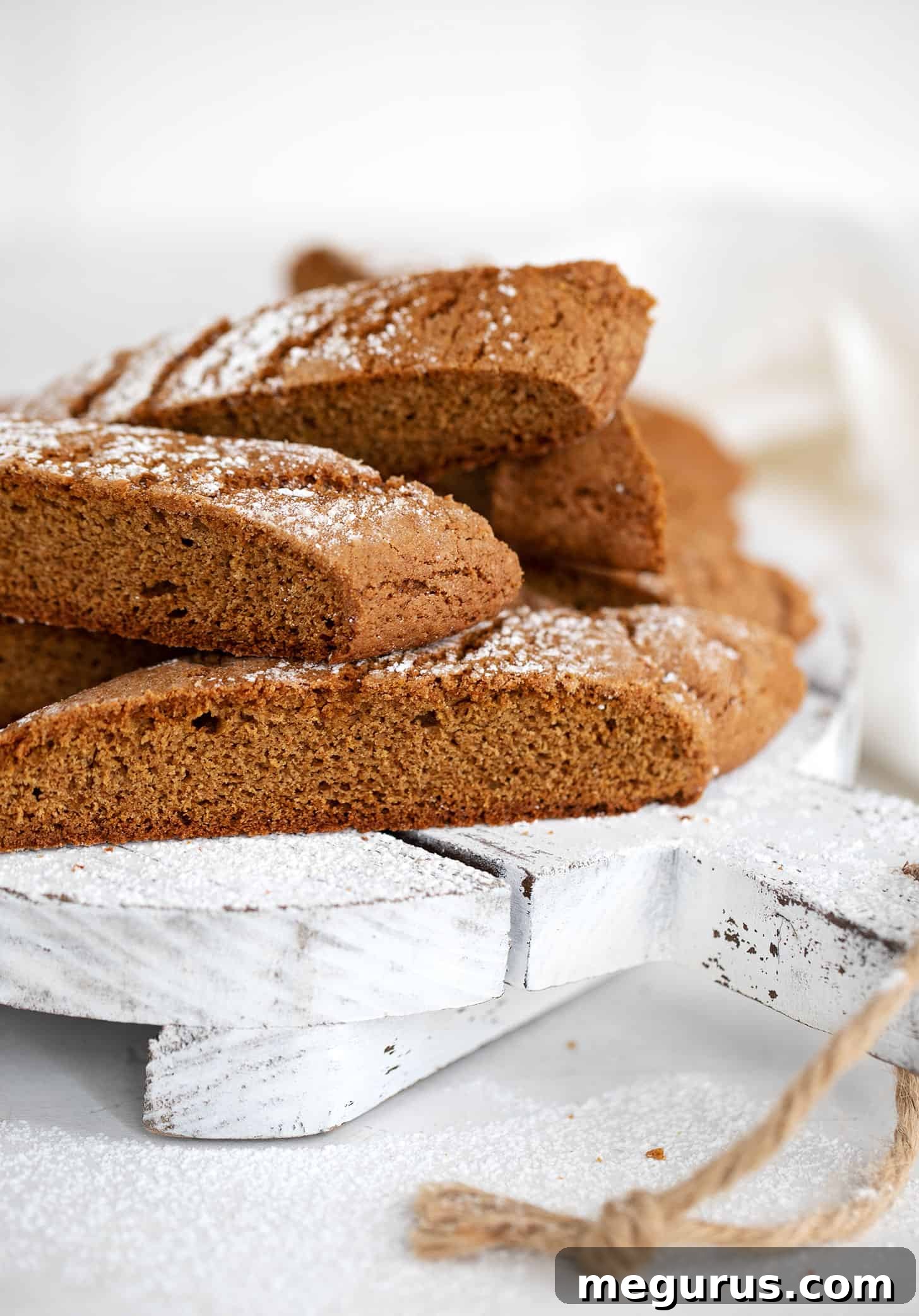 Close-up of baked gingerbread biscotti on a white serving board, showcasing the icing sugar dusting.