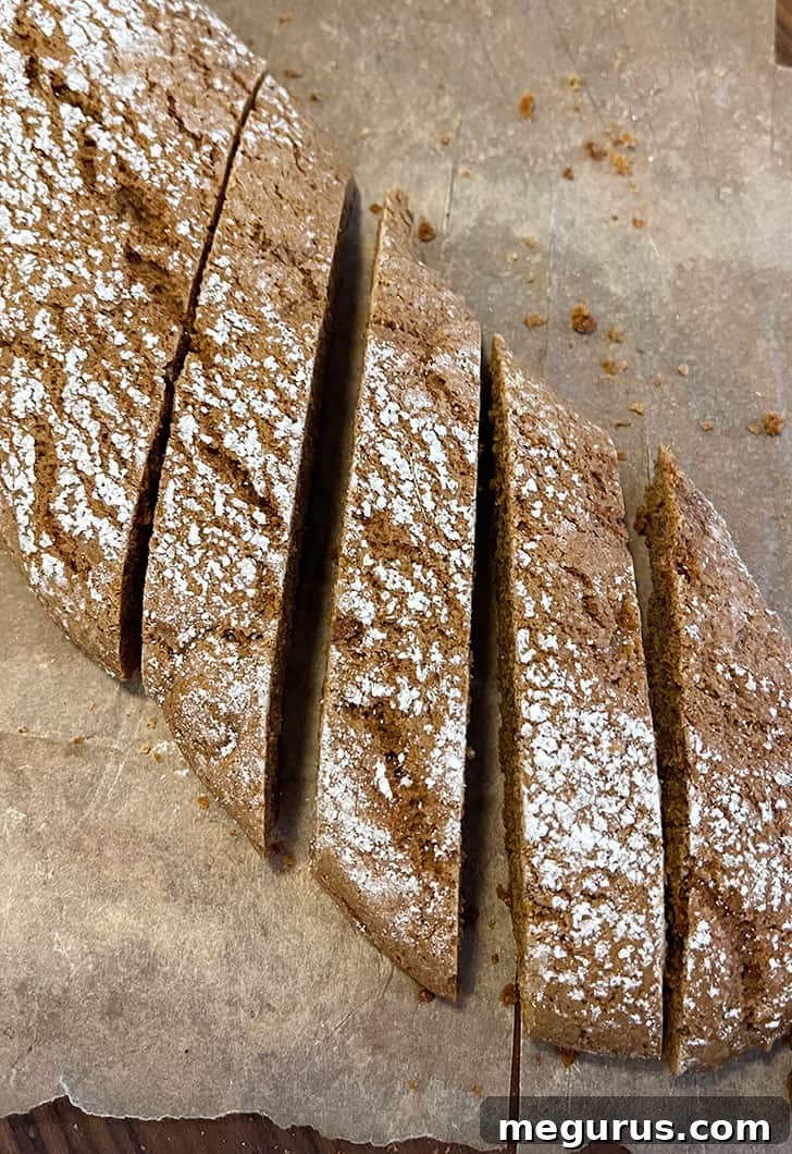 Slicing baked gingerbread biscotti logs with a serrated knife.