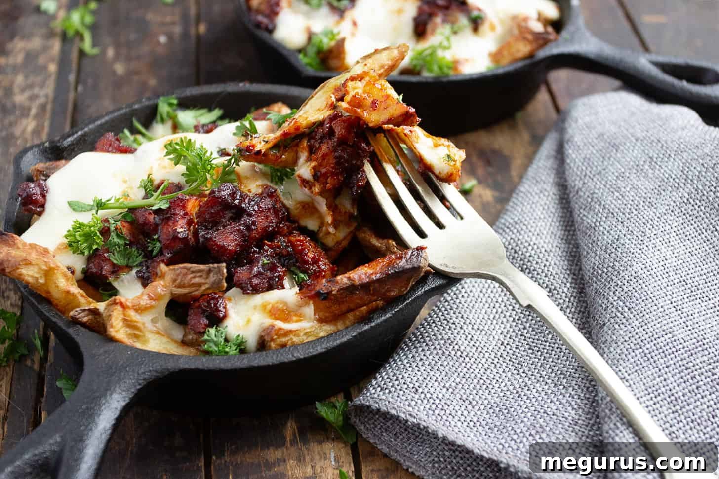 Korean fire chicken cheese fries in small cast iron skillet, golden fries topped with vibrant red chicken and melted white cheese