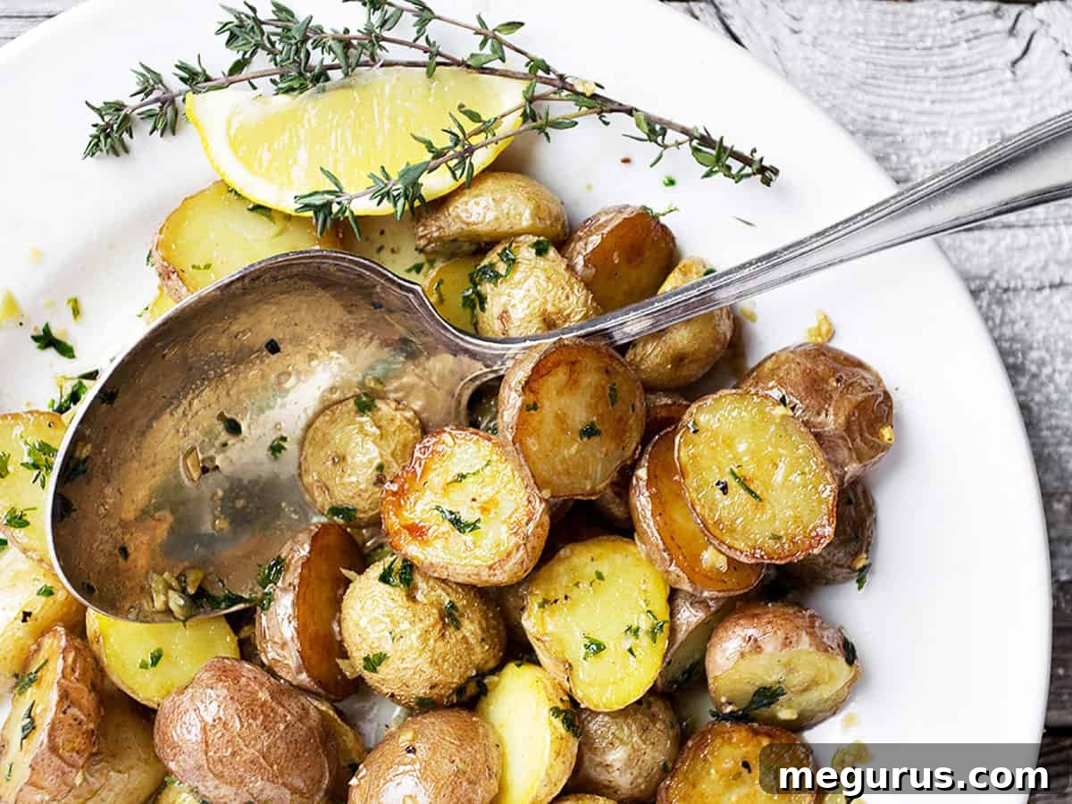 Crispy garlic lemon roasted potatoes served in a white bowl with a spoon, garnished with fresh herbs.