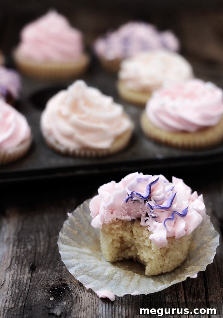 A collection of beautifully decorated classic vanilla cupcakes, some with two-tone pink frosting, on a cooling rack