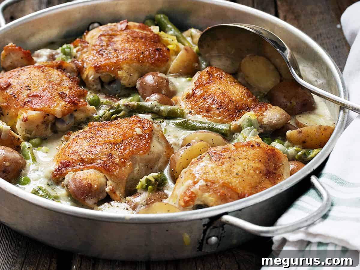 Crispy-skinned chicken thighs with asparagus, mini potatoes, and peas in a creamy sauce, ready to serve.
