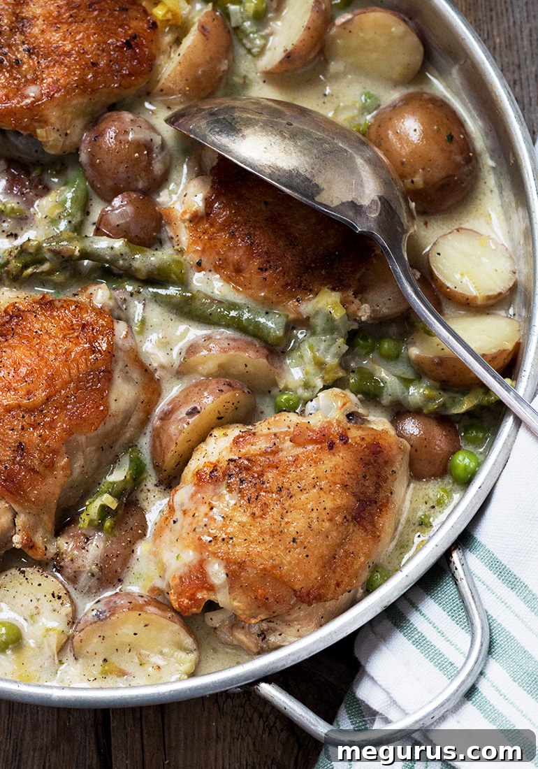 Creamy chicken thighs and asparagus in a rustic skillet, surrounded by tender potatoes and bright green peas, ready to be served.