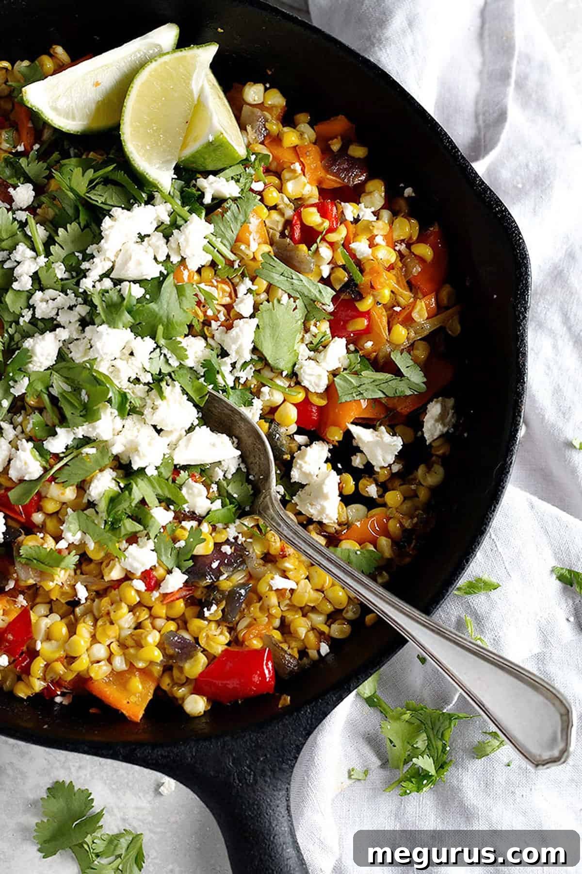 Close-up of skillet roasted corn and bell peppers with crumbled feta cheese, garnished with fresh cilantro and lime wedges