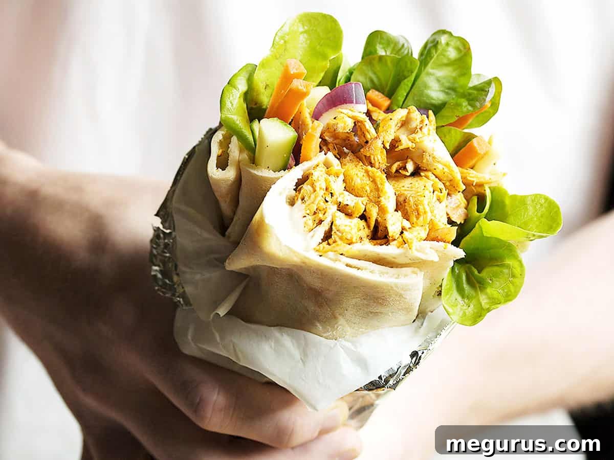 Hand holding a perfectly wrapped chicken shawarma pita with fresh ingredients visible