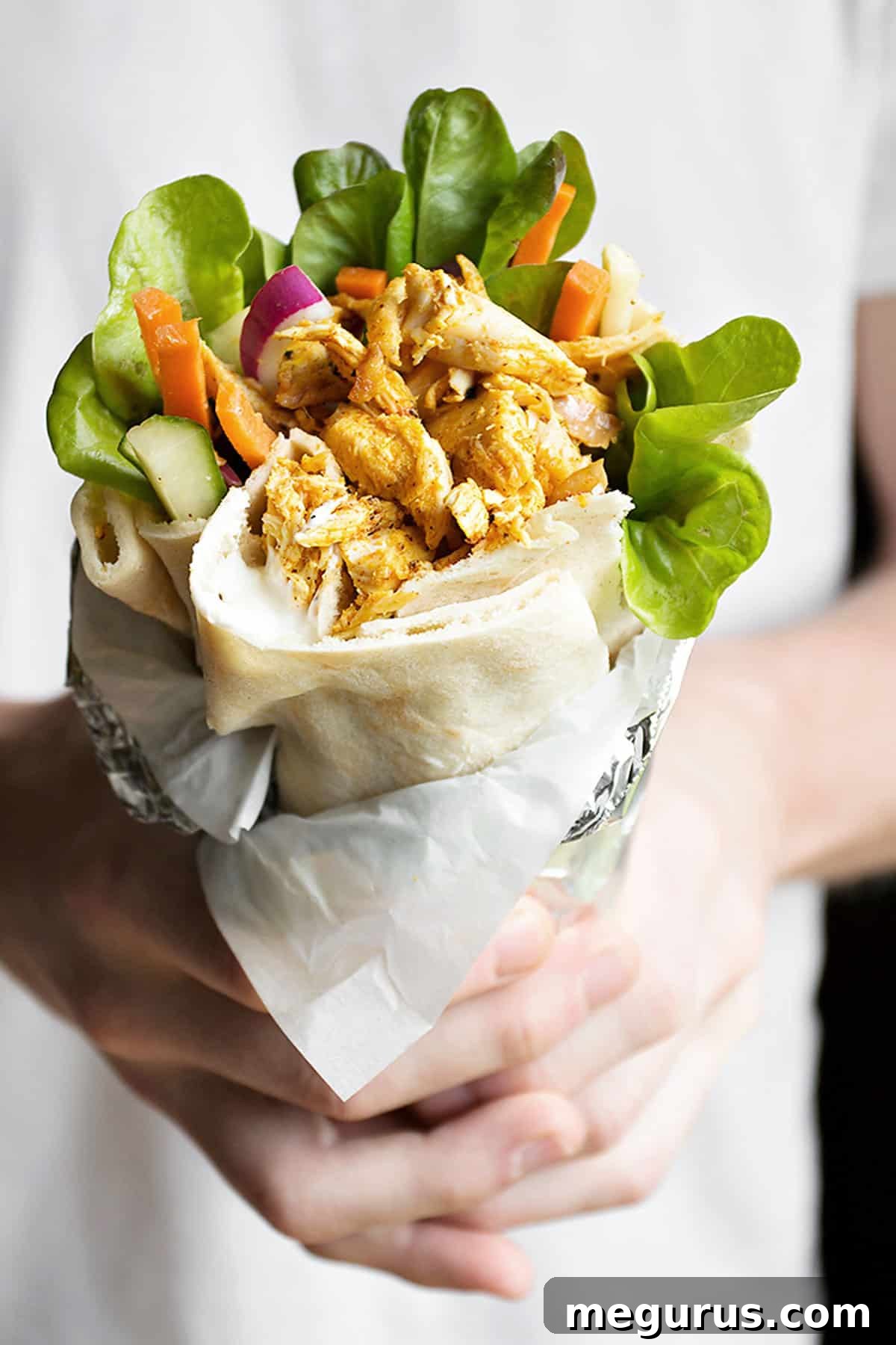 Close-up of a chicken shawarma pita wrap, showing the spiced chicken, fresh vegetables, and creamy sauce peeking out